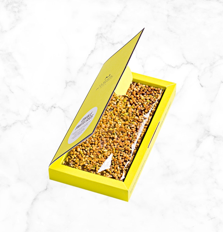 A crunchy mixture of almonds, pistachios and hazelnuts on a thin layer of dark chocolate, creating the perfect bar to share, presented in an elegant and brightly colored box.