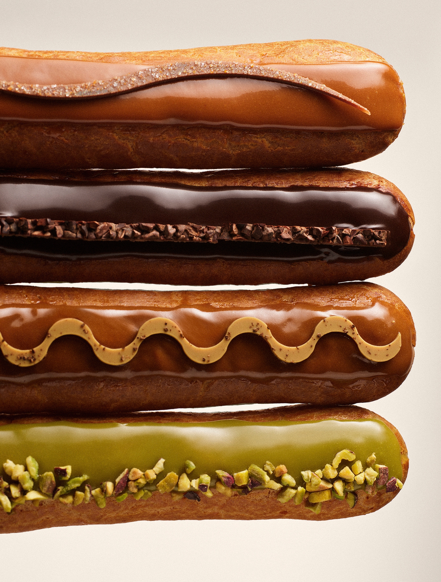 various maison eclairs arranged in row with flavors of chocolate, caramel, coffee, and pistachio displayed against a beige background